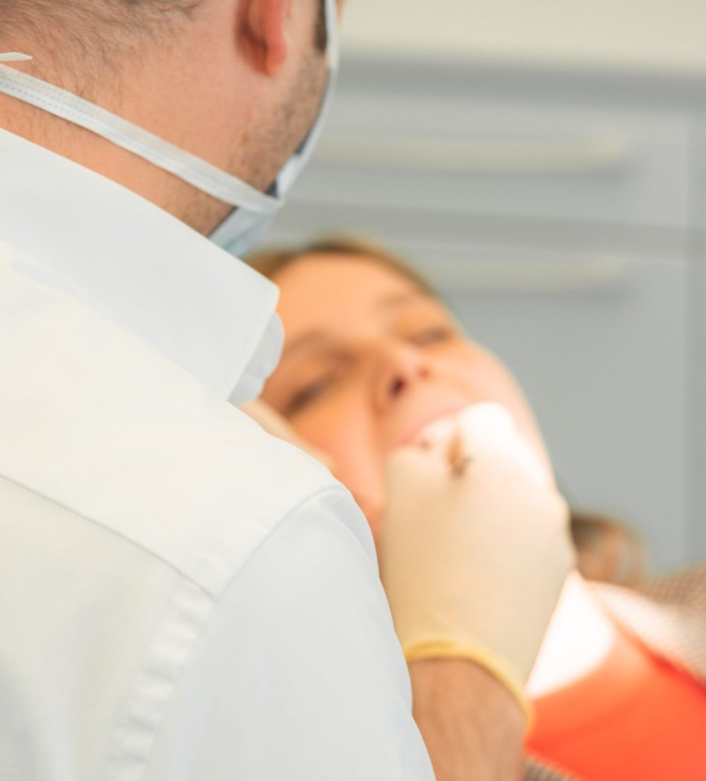 Entspannte Patientin mit geschlossenen Augen während der Behandlung, im Vordergrund der Zahnarzt